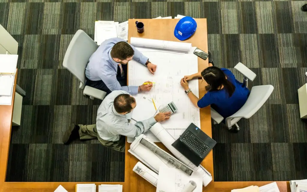 Three land professionals reviewing commercial real estate construction blueprints on a desk